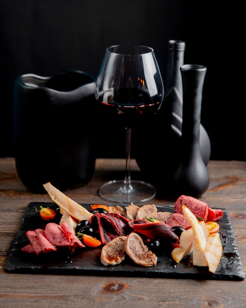 Plato de carne con aceitunas y tomates servidos con copa de vino