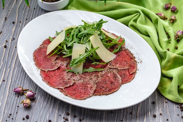 Plato de carne ahumada sobre la mesa con especias rúcula parmesano vista lateral