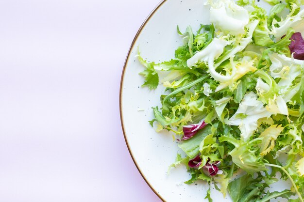 Plato de cerámica blanca con ensalada fresca sobre superficie rosa claro