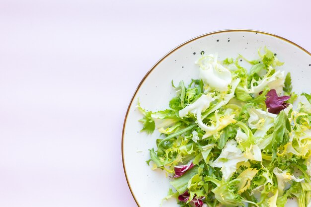 Plato de cerámica blanca con ensalada fresca sobre superficie rosa claro