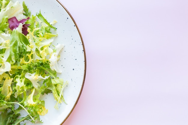 Plato de cerámica blanca con ensalada fresca sobre superficie rosa claro