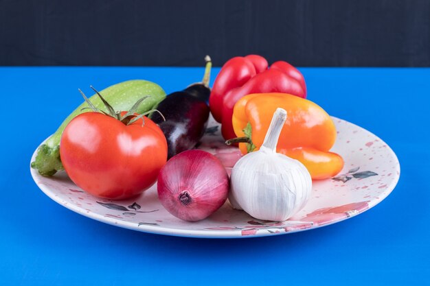 Plato colorido de verduras frescas maduras sobre superficie azul