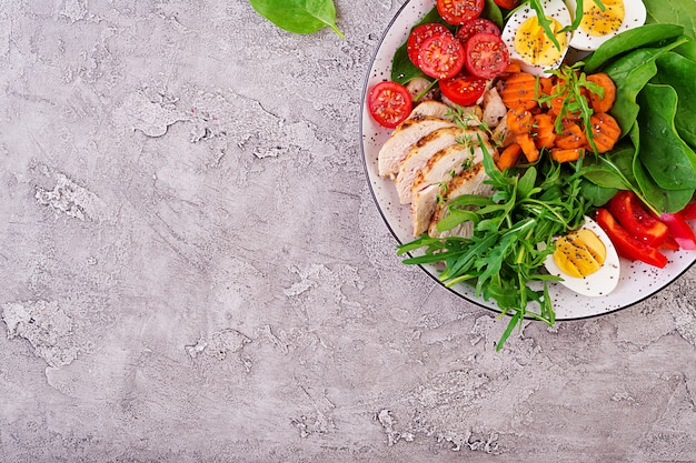 Plato con una comida de dieta ceto. Tomates cherry, pechuga de pollo, huevos, zanahoria, ensalada con rúcula y espinacas. Keto almuerzo. Vista superior