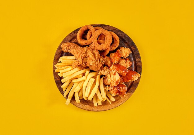 Plato de comida rápida sobre fondo amarillo. Conjunto de comida rápida pollo frito y papas fritas. Comida rápida para llevar. Vista superior. Copie el espacio. Naturaleza muerta. Endecha plana.