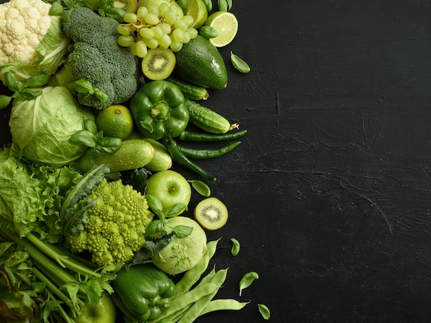 Plato de comida sana sobre fondo de piedra negra. Conjunto saludable que incluye verduras y frutas. Uva, manzana, kiwi, pimiento, lima, repollo, calabacín, pomelo. Nutrición adecuada o menú vegetariano.