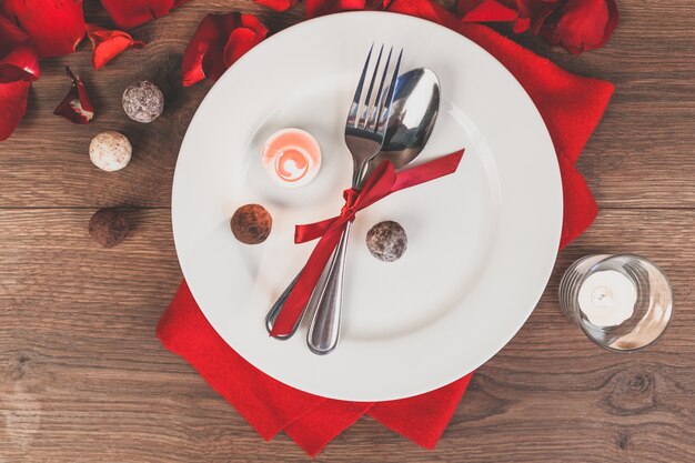 Plato con cubiertos enrollados en un lazo rojo y pétalos de rosa