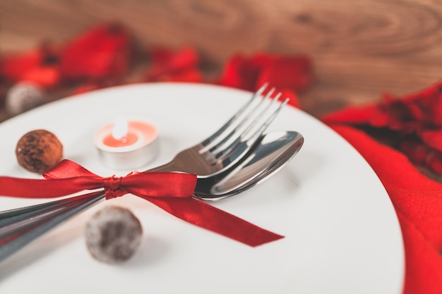 Plato con cubiertos enrollados en un lazo rojo y pétalos de rosa