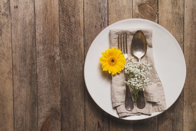 Plato con cubiertos y flor sobre mesa de madera