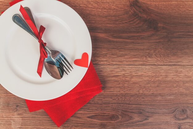 Plato con cubiertos con un lazo rojo y un corazón