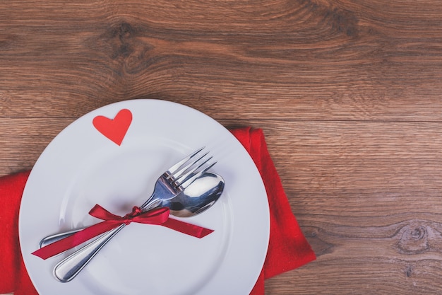 Plato con cubiertos con un lazo rojo y un corazón