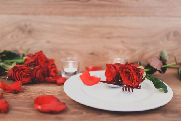 Plato con cubiertos y rosas y velas encendidas de fondo