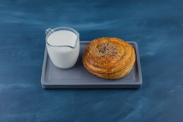 Plato de deliciosa pastelería con semillas negras y vaso de leche sobre superficie azul.