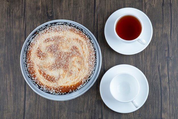 Un plato de delicioso pastel con una taza de té negro colocado sobre una mesa de madera.