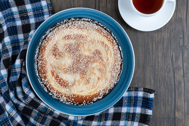 Un plato de delicioso pastel con una taza de té negro colocado sobre una mesa de madera.