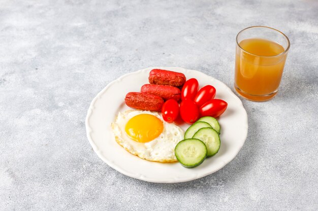 Un plato de desayuno que contiene salchichas tipo cóctel, huevos fritos, tomates cherry, dulces, frutas y un vaso de jugo de durazno.