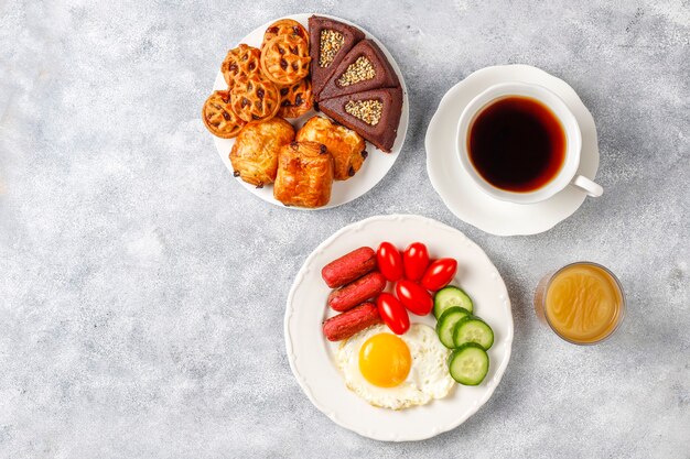 Un plato de desayuno que contiene salchichas tipo cóctel, huevos fritos, tomates cherry, dulces, frutas y un vaso de jugo de durazno.