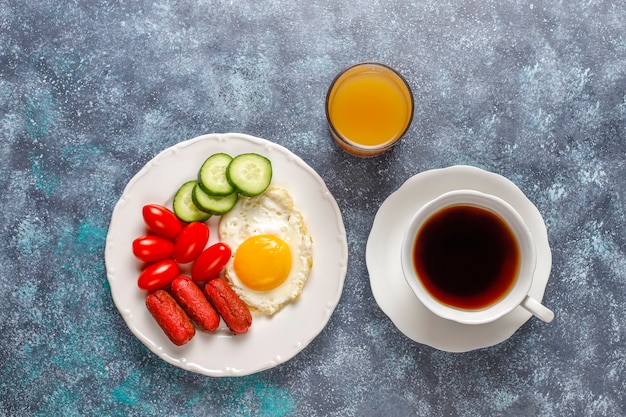 Un plato de desayuno que contiene salchichas tipo cóctel, huevos fritos, tomates cherry, dulces, frutas y un vaso de jugo de durazno.