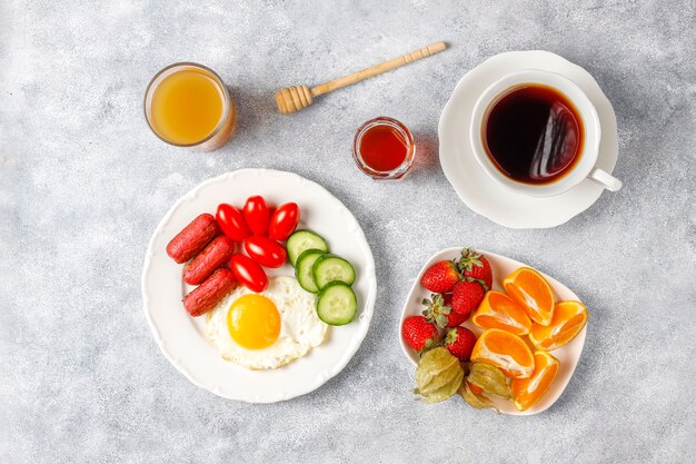 Un plato de desayuno que contiene salchichas tipo cóctel, huevos fritos, tomates cherry, dulces, frutas y un vaso de jugo de durazno.