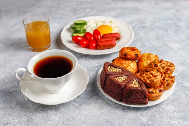 Un plato de desayuno que contiene salchichas tipo cóctel, huevos fritos, tomates cherry, dulces, frutas y un vaso de jugo de durazno.