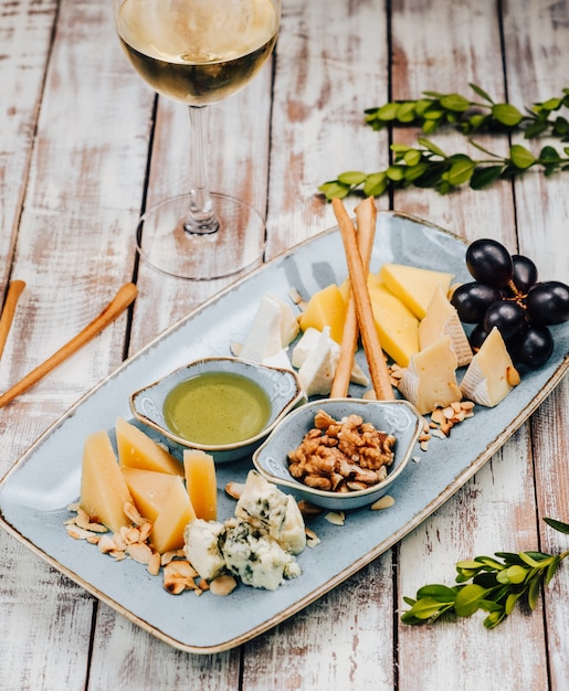 Plato con diferentes quesos y uvas, y copa de vino blanco.