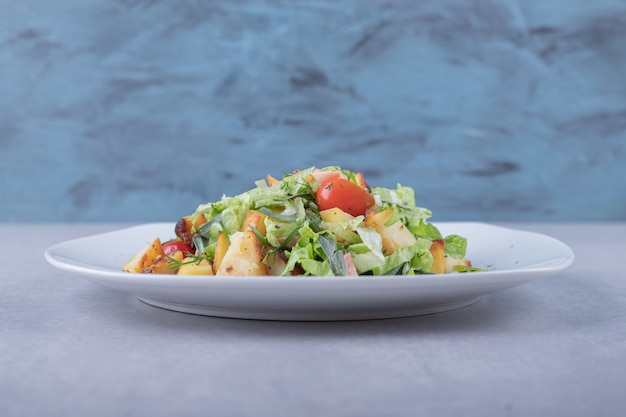 Plato de ensalada fresca con salchichas sobre fondo de piedra.