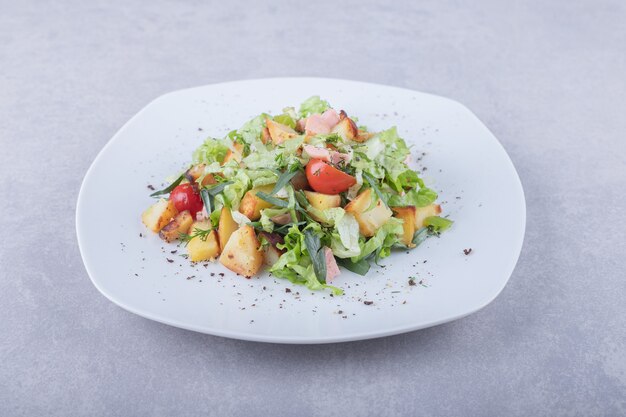 Plato de ensalada fresca con salchichas sobre fondo de piedra.