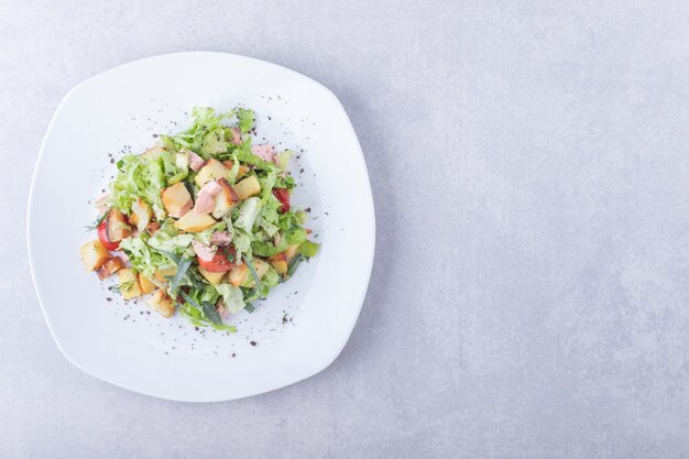 Plato de ensalada fresca con salchichas sobre fondo de piedra.