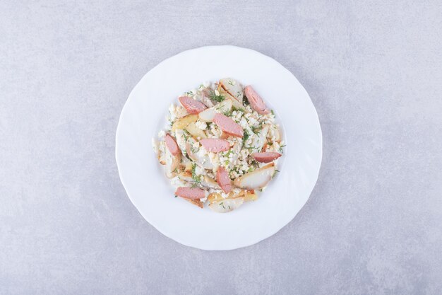 Plato de ensalada con salchichas sobre fondo de piedra.