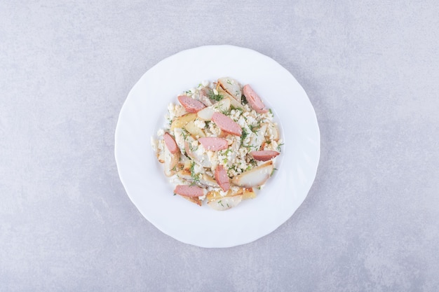 Plato de ensalada con salchichas sobre fondo de piedra.