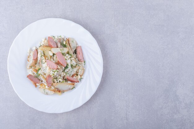 Plato de ensalada con salchichas sobre fondo de piedra.