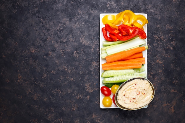 Plato de ensalada de verduras orgánicas frescas con hummus sobre una superficie de hormigón o marrón oscuro
