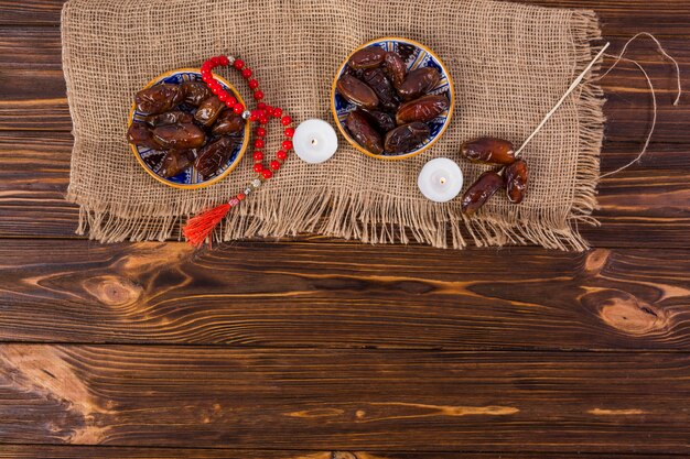 Plato de fechas jugosas con cuentas de oración rojas y vela encendida en el escritorio de madera