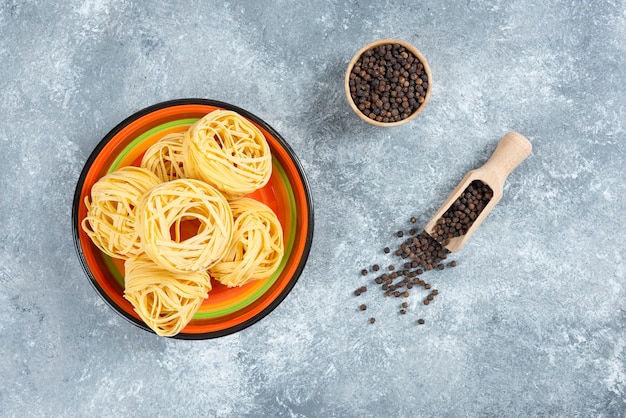 Plato de fideos y granos de pimienta sobre fondo de mármol.