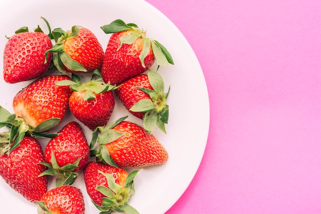 Plato de fresas sobre fondo rosa