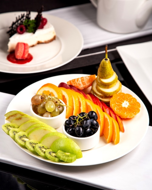 Plato de frutas con kiwi verde manzana uvas naranja y pera