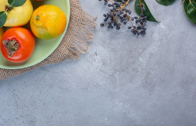 Plato de frutas variadas sobre un trozo de tela sobre fondo de mármol.