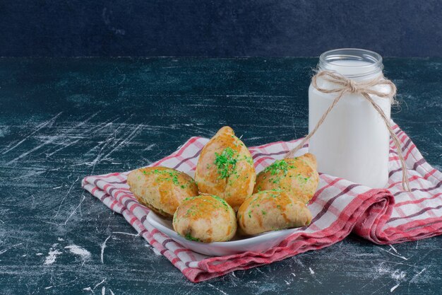 Plato de galletas caseras y tarro de leche en la mesa de mármol.