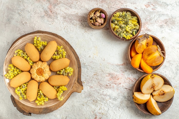 Un plato de galletas y diferentes flores y frutos secos sobre suelo de mármol