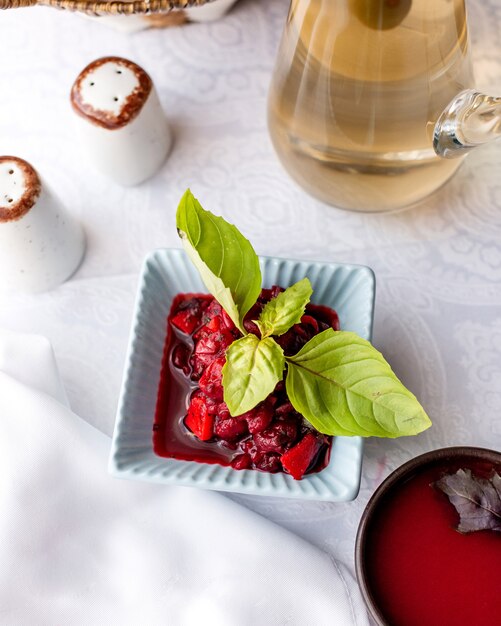 Un plato de guarnición con vegetales rojos cocidos cubiertos con albahaca