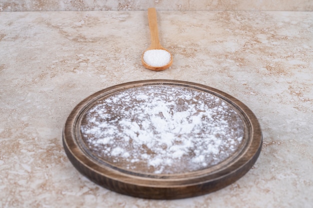 Un plato de harina marrón y una cuchara de madera de azúcar.