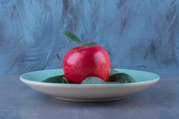 Un plato de hojas con manzana sobre la superficie oscura.