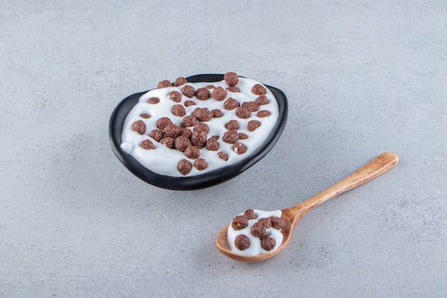 Un plato hondo negro de leche con cereales de chocolate y cuchara de madera. Foto de alta calidad