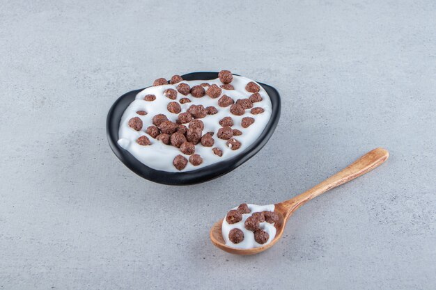 Un plato hondo negro de leche con cereales de chocolate y cuchara de madera. Foto de alta calidad