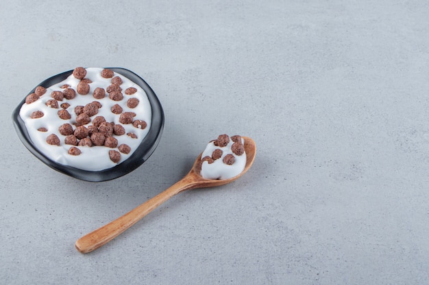 Un plato hondo negro de leche con cereales de chocolate y cuchara de madera