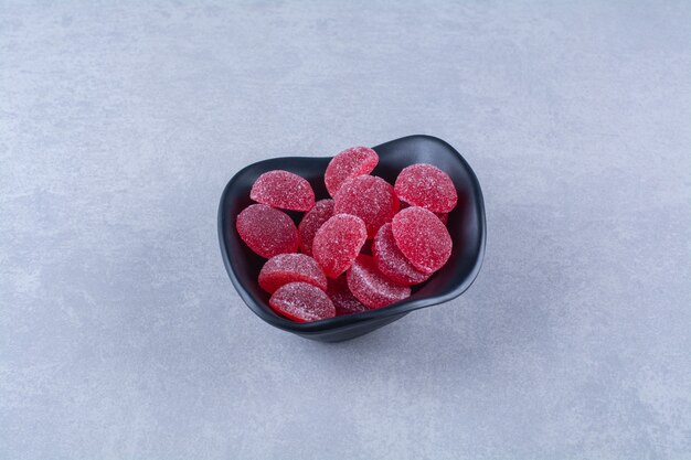 Un plato hondo negro lleno de caramelos de gelatina de frutas azucaradas rojas sobre fondo gris. Foto de alta calidad