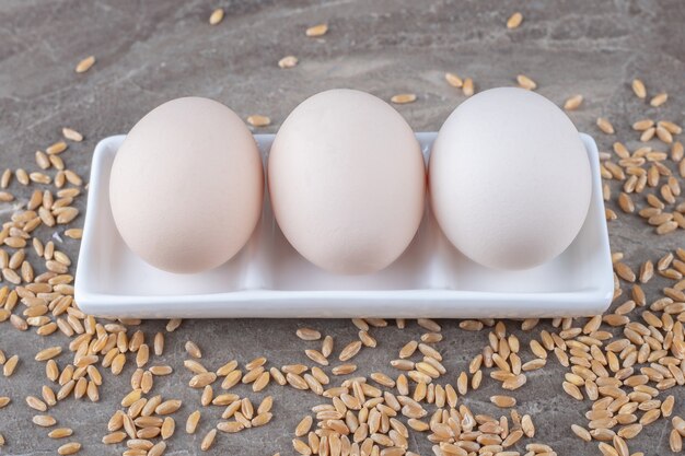 Plato de huevos crudos y cebada sobre fondo de mármol.