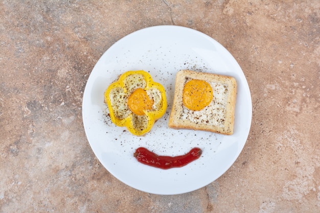 Plato de huevos fritos con tostadas y especias sobre superficie de mármol