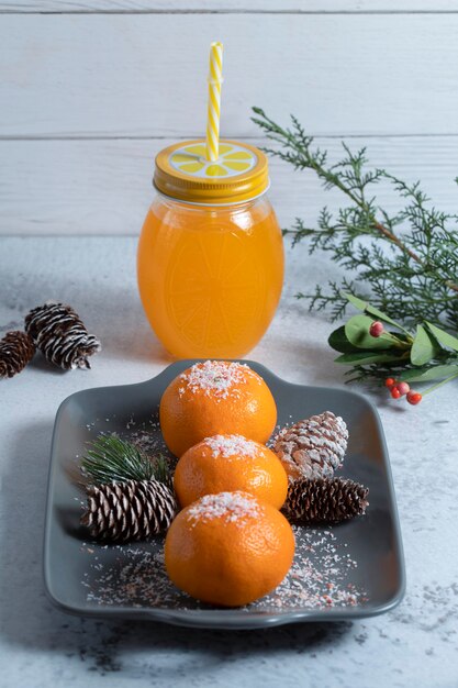 Plato de jugosas mandarinas decorado con polvo y piñas y tarro de jugo.