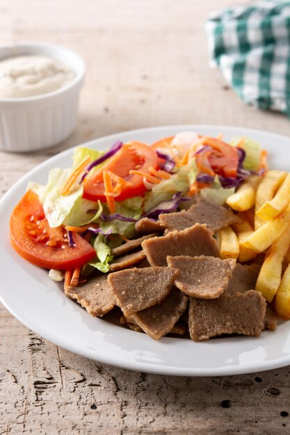 Plato de kebab, verduras y papas fritas en la mesa de madera