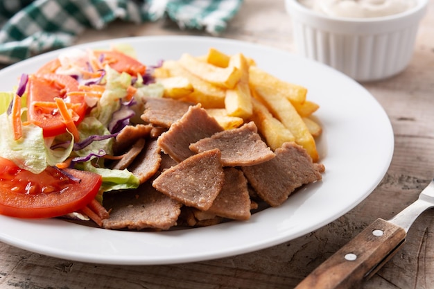 Plato de kebab, verduras y patatas fritas en mesa de madera